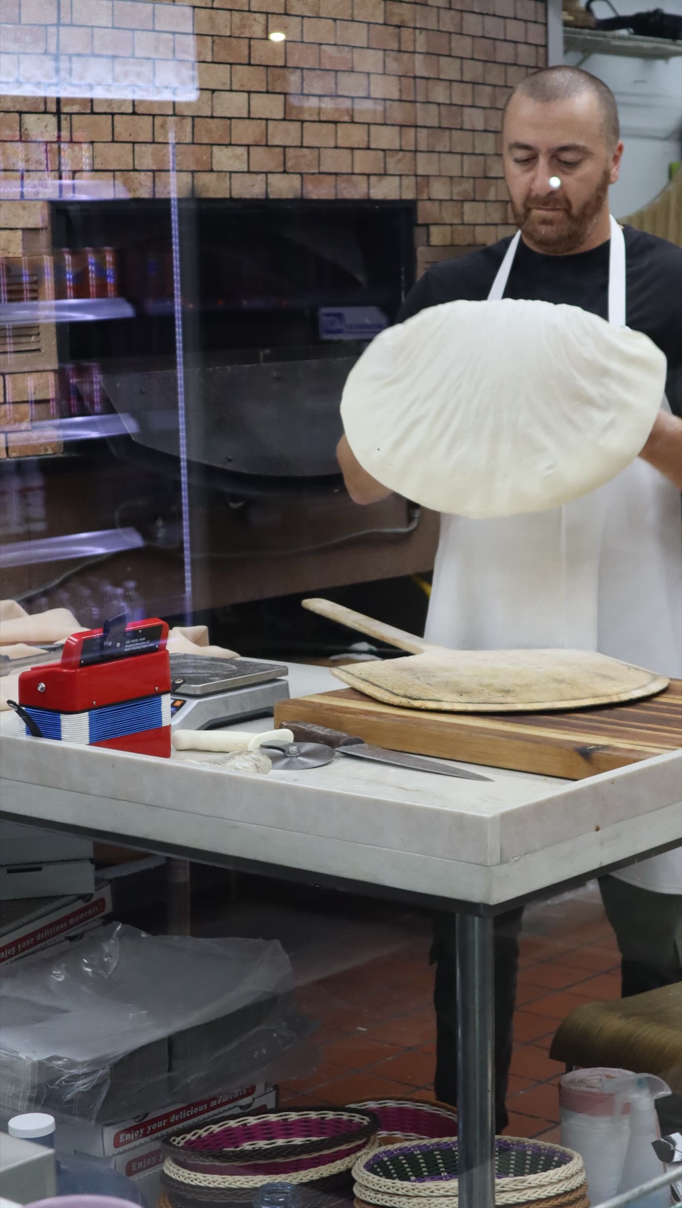 A baker hand-stretching dough at the stone oven